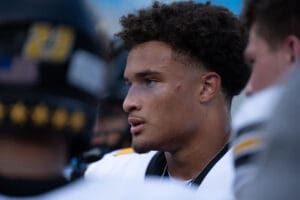 Focused football player on the field, wearing a uniform, with teammates in the background.