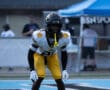 Football player in black and yellow gear focused on the field during a game under clear skies.