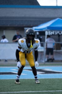 Football player in black and yellow gear focused on the field during a game under clear skies.