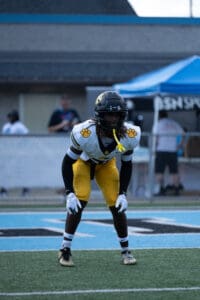 Football player in yellow pants and black helmet prepares on field during game.