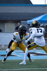 Two football players in black helmets and yellow pants facing off on a field during a game.