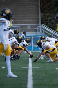 Football players in yellow and white uniforms lining up for the snap on a field, ready for action.