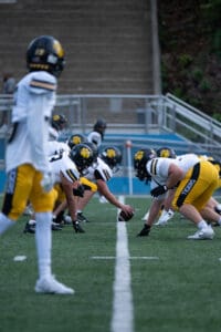 Football players in yellow and black uniforms prepare for a scrimmage on the field during practice.