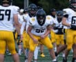 Football players in white and yellow uniforms preparing for a game on the field.