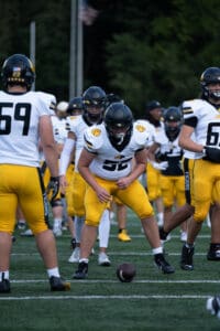 Football players in white and yellow uniforms preparing for a game on the field.