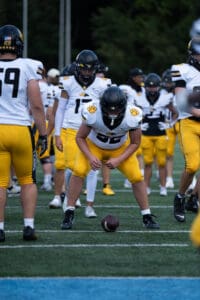 Football players in yellow and white uniforms practicing a snap on the field.