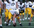 Football players in yellow pants and white jerseys prepare for a play on the field.