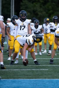 Football players in yellow pants and white jerseys prepare for a play on the field.