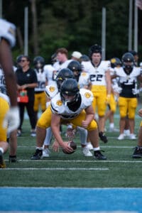 Football players in yellow and white uniforms prepare for a snap during a game on a green field.
