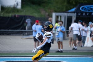Football player in yellow pants and black helmet scoring a touchdown on the field during a game.