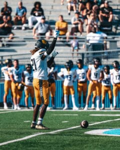 Football player signaling on the field as teammates watch in the background during a game.