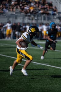 Football player in yellow Tigers uniform running with ball on the field during a game.
