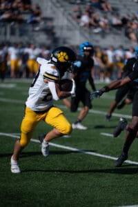 Football player in yellow pants running with the ball, dodging opponents on a sunny field.