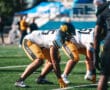 Football players in action on the field during a sunny game day wearing blue and gold uniforms.