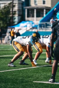 Football players in action on the field during a sunny game day wearing blue and gold uniforms.