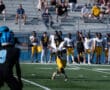 Football player in white and yellow uniform catching ball during a game, with spectators in the stands.