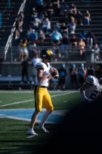 Football player in yellow pants preparing to throw a pass during a game, with crowd in background.