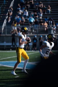 Quarterback prepares to throw a football during a high school game, wearing a yellow jersey and helmet.
