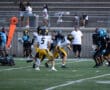 High school football game action with players in yellow and black uniforms running on field.