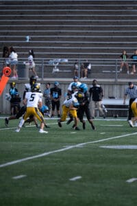 Football game with players tackling on the field, surrounded by spectators in the stands.