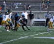High school football game with players tackling on the field, empty bleachers in the background.