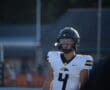 High school football player in black helmet and white jersey with number 4, focused on the game.