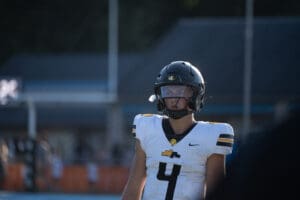 High school football player in black helmet and white jersey with number 4, focused on the game.