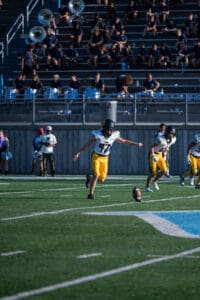 Football player kicks off under the bright lights, band and cheerleaders in the background. Game day action.