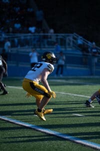 Football player in yellow gear crouches on field under stadium lights, ready to make a move.