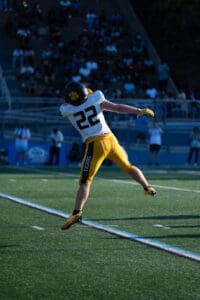 Football player #22 in mid-air catch during a game, wearing a yellow and black uniform on the field.