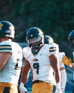 Football players in yellow and white uniforms celebrating on the field.