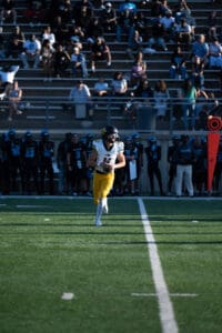 Football player in yellow pants running with ball on field during a game, stadium crowd in background.