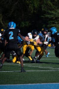 High school football game action with players in yellow and black jerseys running through defenders in blue and black.
