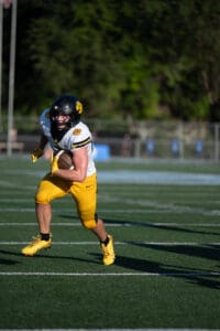 Football player in yellow uniform running with the ball on a field during a game.