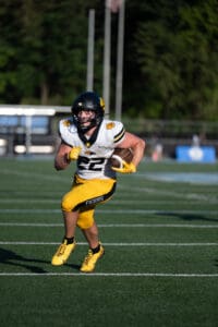 Football player in Tigers uniform running with football on a sunny field.