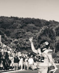Football player celebrating a touchdown on the field, fans cheering in the background.