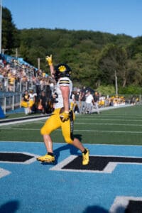 Football player celebrates touchdown with raised hand in end zone during outdoor game.