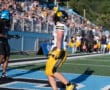 Football player in yellow uniform celebrates a touchdown on a sunny day at a packed stadium.