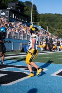 Football player in yellow uniform celebrates a touchdown on a sunny day at a packed stadium.