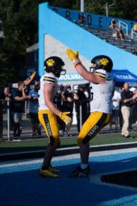 Football players in yellow Tiger uniforms celebrate with a high-five in an end zone.