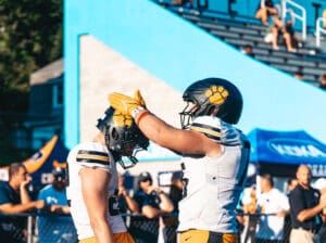 Two football players in helmets, celebrating with a high five on the field.