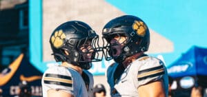 Two football players in matching helmets and jerseys celebrate during a game, showing excitement and teamwork.
