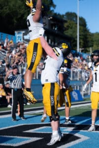 Football players celebrate a touchdown on the field, wearing black and yellow Tigers uniforms.