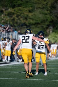 Football players in yellow celebrate a play on the field during a sunny day game.