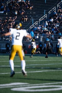 Football players in action on the field with spectators in the stadium stands.