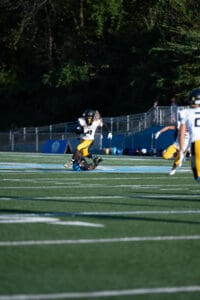 Football player in white and yellow dodges tackle on green field during a sunny game.