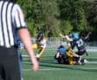 High school football game action with players tackling and referee observing on field.