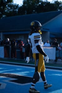 Football player in black and yellow uniform on field, spectators in background.