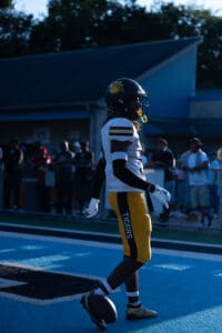 Football player in mid-stride on field, wearing yellow pants and helmet, with fans in the background.