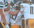 Football players in uniforms celebrate a victory with high fives and hugs on the field.